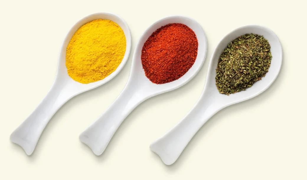 Three spoons heaped with turmeric, chilli and herbs, representing typical usage with other spices